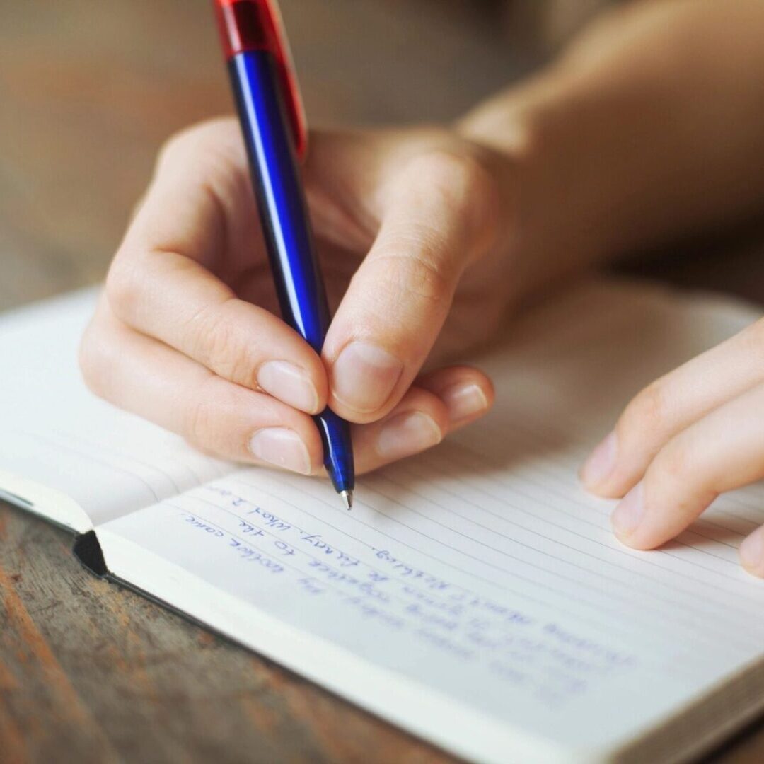 A person writing in a notebook with a pen.